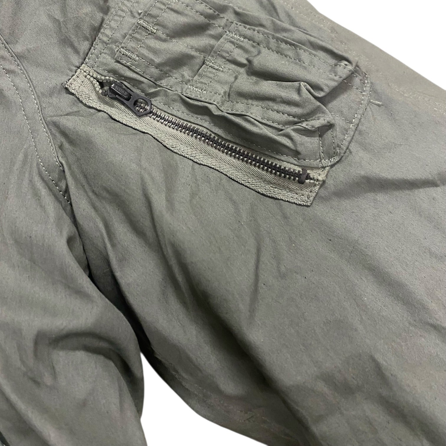 Parka kaki avec poche zippée sur la poitrine à double couture, plumet et fermetures visibles.