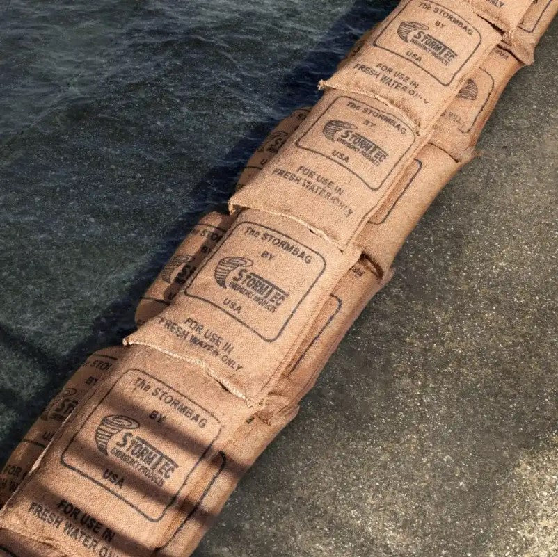 Sacs étanches en carton imprimé “The Stormbag” alignés sur le sol mouillé, destinés à une utilisation contre les inondations. Stormbag – Sac anti-inondation haute performance.