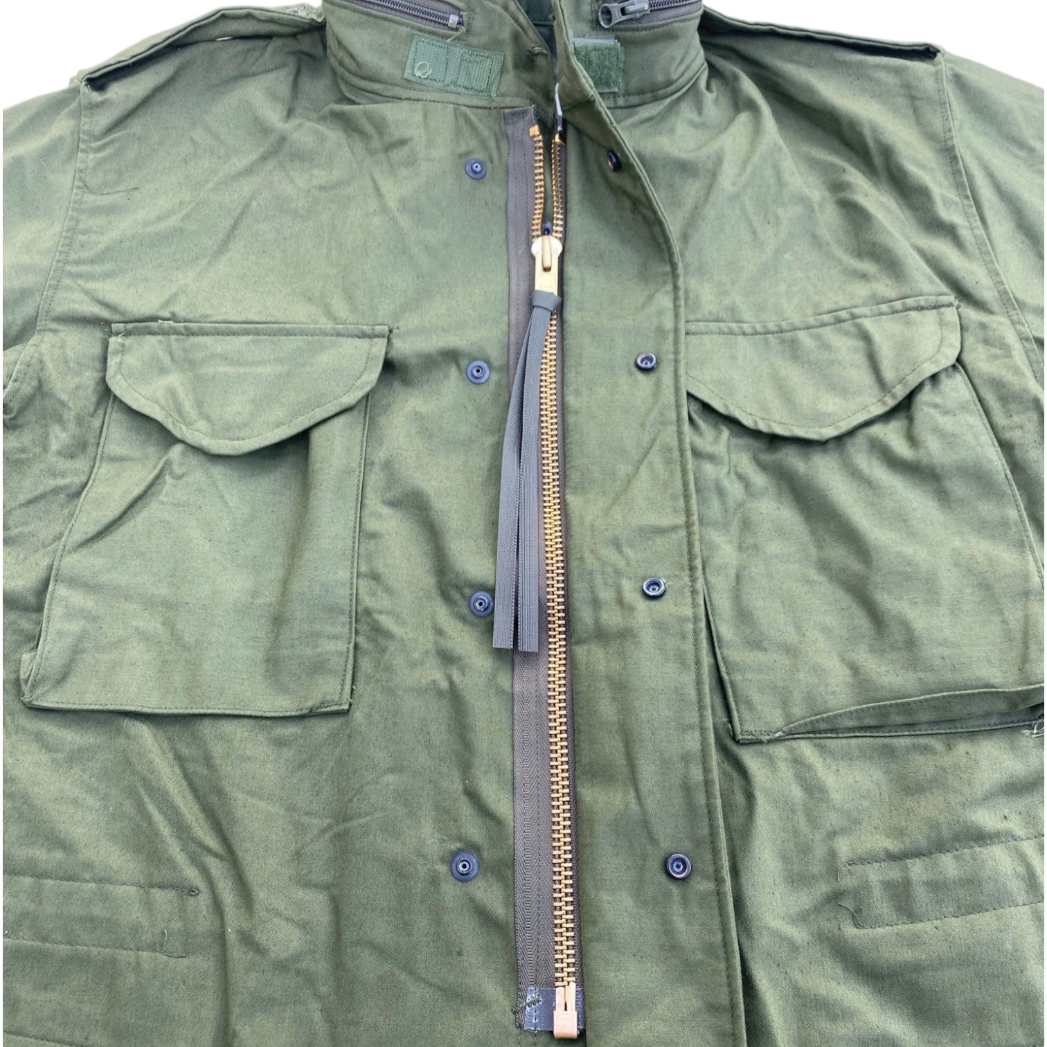 Veste militaire kaki M-65 US Army, fermeture zippée centrale avec zip beige, poches poitrine à rabats et boutons, col haut militaire.