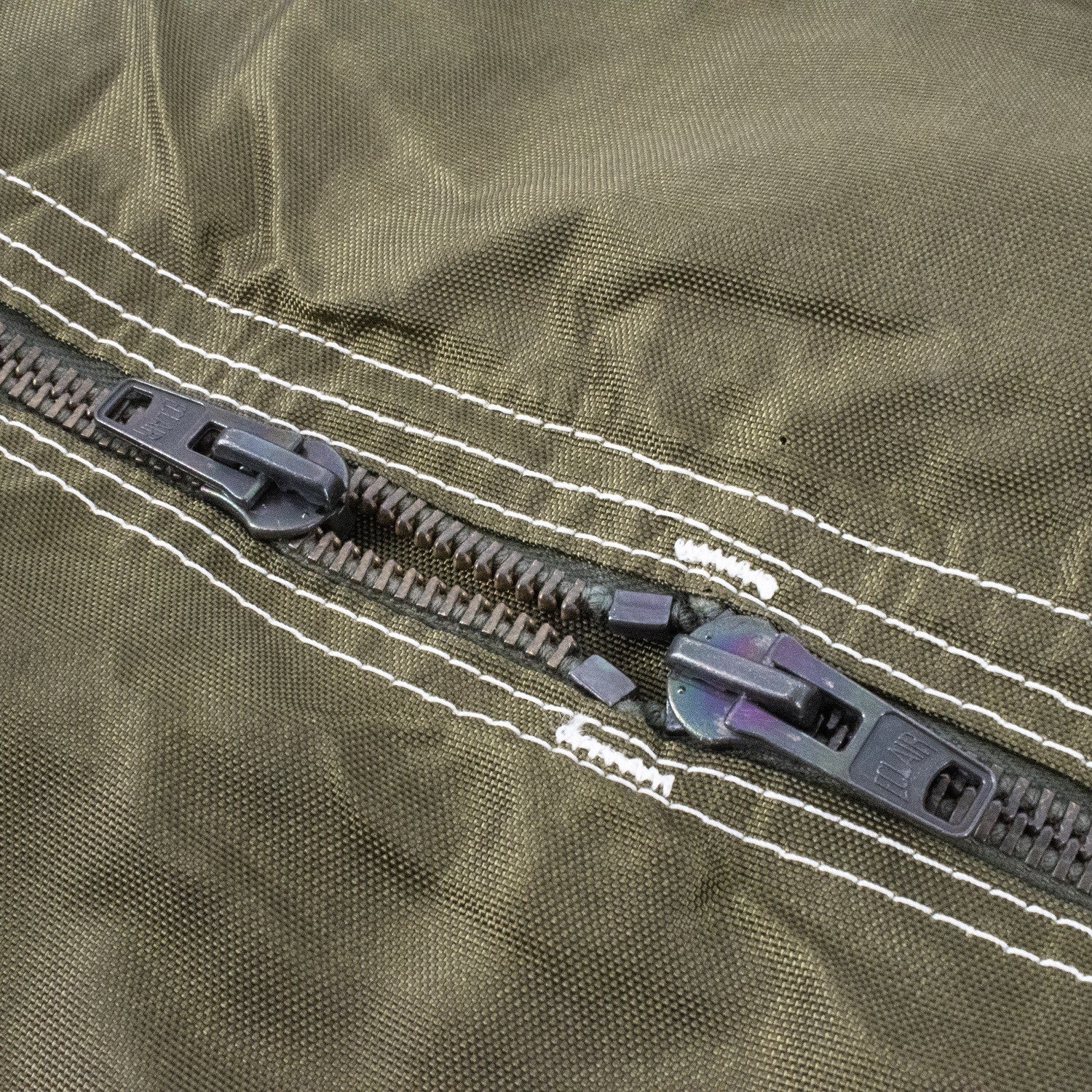 Couture et fermeture éclair doubles sur tissu olive: fermeture éclair centrale avec deux curseurs et drawer, sur sac militaire TAP.