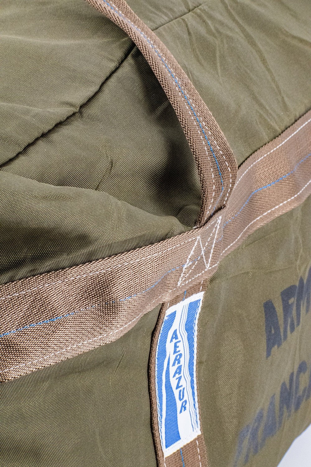 Sac TAP olive avec sangle beige et étiquette bleue, détail de couture et texture robuste.