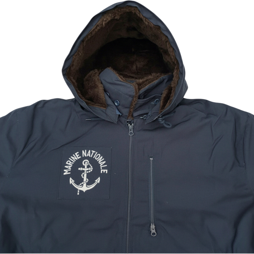Veste marine bleue avec capuche doublée de fourrure synthétique marron, logo Marine Nationale sur la poitrine gauche, fermeture éclair centrale et poche zippée.