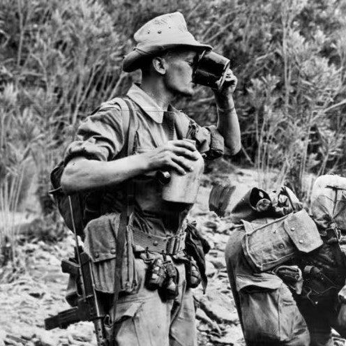 Soldat en uniforme, boîtier alu et gourde près de la poitrine, buvant à partir d’un gobelet en nature. Gourde militaire armée française modèle 52 avec quart.